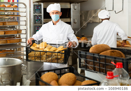 Baker in mask carrying crate with bread 108940186