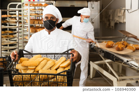 man in chefs uniform with bread in tray in bakery during virus man in chefs uniform with bread in tray in bakery during virus 108940300