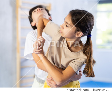 Girls and boys learns to do power grip with trainer during a self-defense lesson in gym Girls and boys learns to do power grip with trainer during a self-defense lesson in gym 108940479