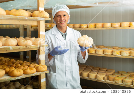 Cheerful cheesemaker standing in ripening room of cheese factory 108940856
