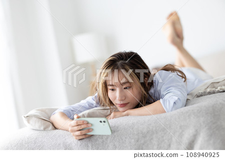 美女:一個女人躺在床上看著她的智慧型手機 美女:一個女人躺在床上看著她的智慧型手機 108940925