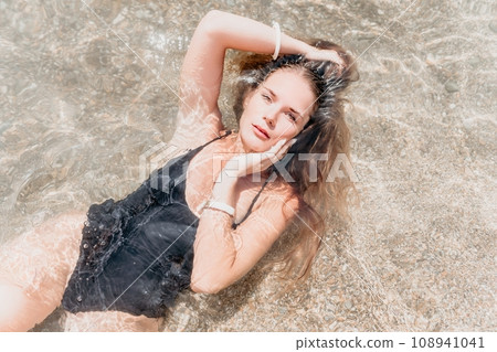 Woman summer travel sea. Happy tourist enjoy taking picture outdoors for memories. Woman traveler posing on the beach at sea surrounded by volcanic mountains, sharing travel adventure journey 108941041