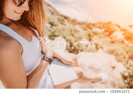 Digital nomad, woman in the hat, a business woman with a laptop sits on the rocks by the sea during sunset, makes a business transaction online from a distance. Freelance, remote work on vacation. Digital nomad, woman in the hat, a business woman with a laptop sits on the rocks by the sea during sunset, makes a business transaction online from a distance. Freelance, remote work on vacation. 108941071