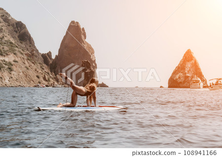 Woman sea sup. Close up portrait of happy young caucasian woman with long hair looking at camera and smiling. Cute woman portrait in bikini posing on sup board in the sea Woman sea sup. Close up portrait of happy young caucasian woman with long hair looking at camera and smiling. Cute woman portrait in bikini posing on sup board in the sea 108941166