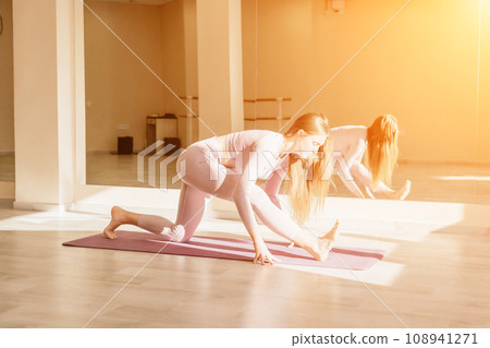 Young sporty woman, fitness instructor in pink sportswear doing stretching and pilates on yoga mat in the studio with mirror. Female fitness yoga routine concept. Healthy lifestyle and harmony. Young sporty woman, fitness instructor in pink sportswear doing stretching and pilates on yoga mat in the studio with mirror. Female fitness yoga routine concept. Healthy lifestyle and harmony. 108941271