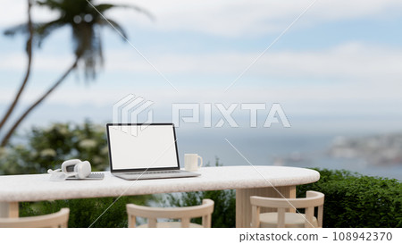 A white-screen laptop mockup, headphone, and a coffee cup on a table on a balcony with a nature view A white-screen laptop mockup, headphone, and a coffee cup on a table on a balcony with a nature view 108942370
