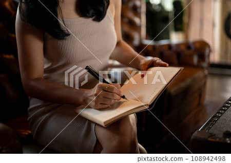 Young elegant Asian woman writing on notebooks in her free time while sitting in her luxury sofa. 108942498