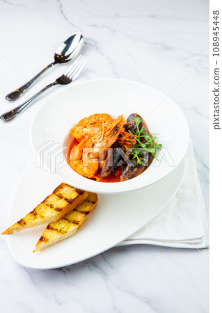 shrimp and mussels with herbs in a white plate with toasted bread, side view 108945448