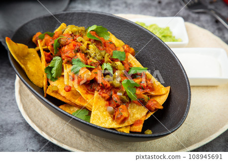 nachos with sauce, meat and herbs in a black plate, side view nachos with sauce, meat and herbs in a black plate, side view 108945691