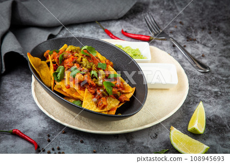 nachos with sauce, meat and herbs in a black plate, side view nachos with sauce, meat and herbs in a black plate, side view 108945693