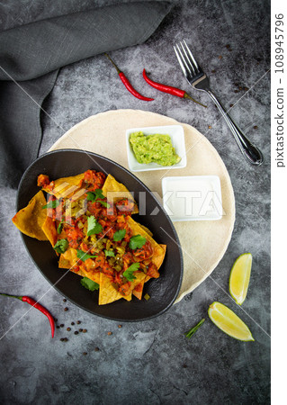 nachos with sauce, meat and herbs in a black plate, top view 108945796
