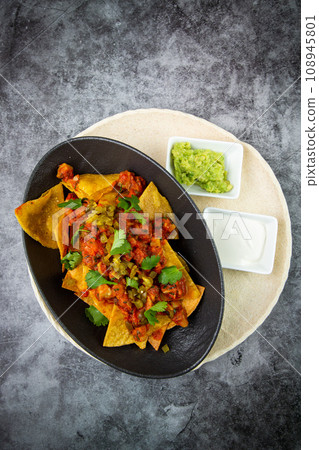 nachos with sauce, meat and herbs in a black plate, top view 108945801
