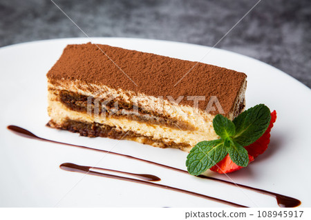 sponge cake filled with strawberries, mint and chocolate syrup on a white plate side view 108945917