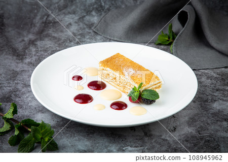 white sponge cake with drops of syrup, mint and wild berries on a round plate side veiw 108945962