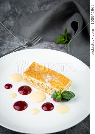 white sponge cake with drops of syrup, mint and wild berries on a round plate side veiw 108945963