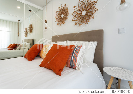 Double bed in the bright bedroom room interior furnishing furniture. Red decorative pillows and lamp shades in the foreground. Double bed in the bright bedroom room interior furnishing furniture. Red decorative pillows and lamp shades in the foreground. 108948008