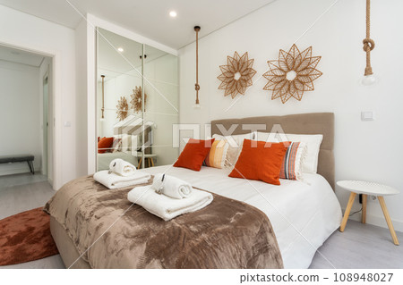 Double bed in the bright bedroom room interior furnishing furniture. Velour brown comforter with towels aromatic herbs and a closet with mirror. Double bed in the bright bedroom room interior furnishing furniture. Velour brown comforter with towels aromatic herbs and a closet with mirror. 108948027
