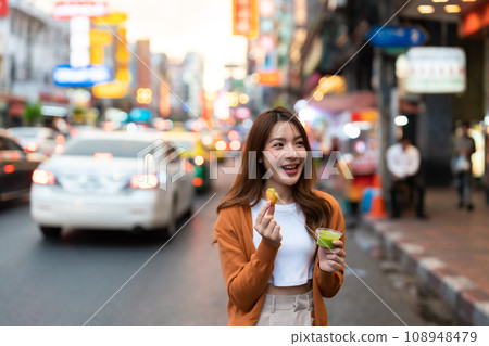 Young Asian tourists standing and eating Thai desserts 108948479