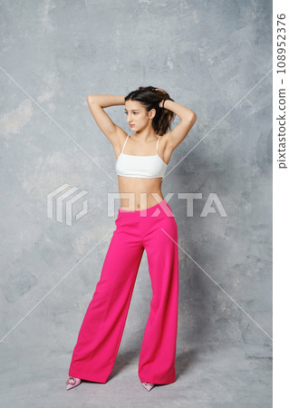 Young woman in wide cherry pink trousers and white tube top pulling hair Young woman in wide cherry pink trousers and white tube top pulling hair 108952376