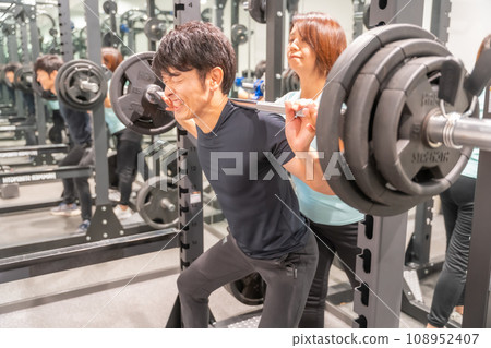 一名男子艱難舉起槓鈴，一名教練協助他 108952407