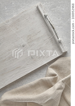 A fragment of a wooden white painted tray and a crumpled linen kitchen towel on a gray concrete table. Top view with copy space A fragment of a wooden white painted tray and a crumpled linen kitchen towel on a gray concrete table. Top view with copy space 108952968