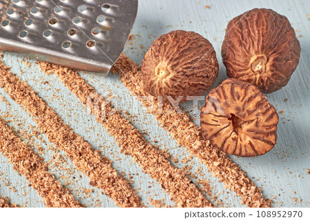 Three nutmegs, a metal grater and trails of nutmeg powder on a wooden table 108952970