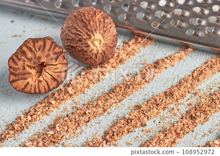 Two nutmegs, a metal grater and trails of nutmeg powder on a wooden table Two nutmegs, a metal grater and trails of nutmeg powder on a wooden table 108952972