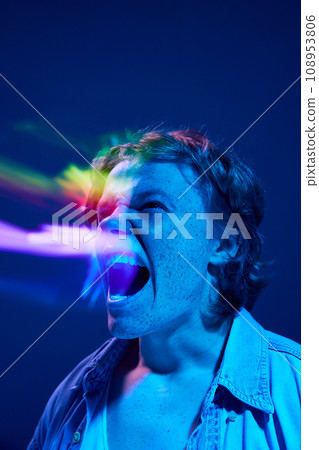 Flow of emotions. Portrait of young man, widely open mouth and aggressively shouting in mixed neon light illuminating futuristic, digital projector reflection. Flow of emotions. Portrait of young man, widely open mouth and aggressively shouting in mixed neon light illuminating futuristic, digital projector reflection. 108953806