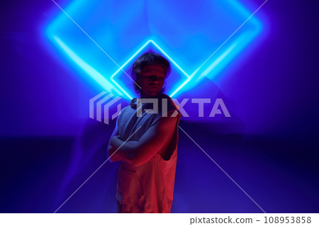 Futuristic portrait of handsome, calm man posing in neon light against background illuminated abstract digital, projector reflection. 108953858