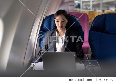 Beautiful businesswoman asian sitting near window on airplane listen music in earphones while working with laptop Beautiful businesswoman asian sitting near window on airplane listen music in earphones while working with laptop 108953929