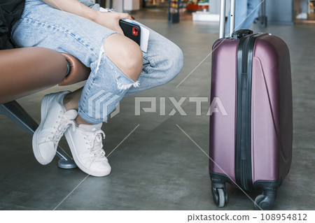 Travel, airport. A woman with a suitcase is waiting for a plane sitting at the airport. Travel, airport. A woman with a suitcase is waiting for a plane sitting at the airport. 108954812