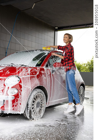 Woman in red checkered shirt washing the car and looking busy 108955018