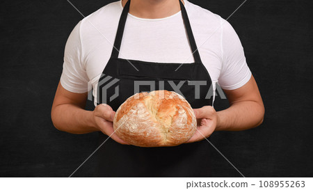 Fresh baked bread in the hands of a baker on a black background. Fresh baked bread in the hands of a baker on a black background. 108955263