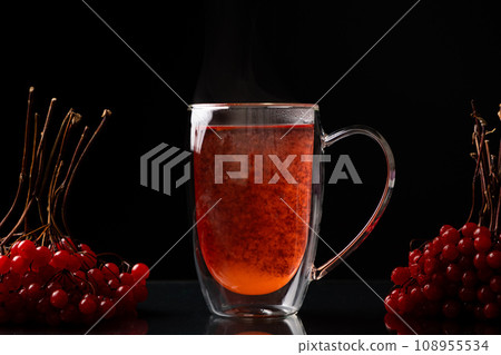 Hot viburnum tea in a glass cup with a double bottom on a black background. Hot viburnum tea in a glass cup with a double bottom on a black background. 108955534