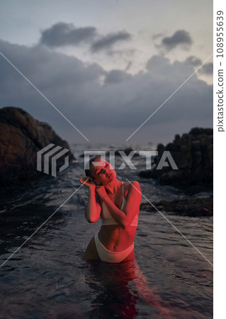 Attractive female enjoys serene night swim in ocean illuminated by red light. Woman relaxes in tranquil sea, beauty and self-care blend with travel. 108955639