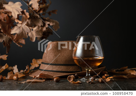 Snifter of brandy on a stone table with dried-up oak leaves. 108958470