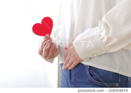 A woman holding a heart object and placing her hand on her lower abdomen A woman holding a heart object and placing her hand on her lower abdomen 108958654