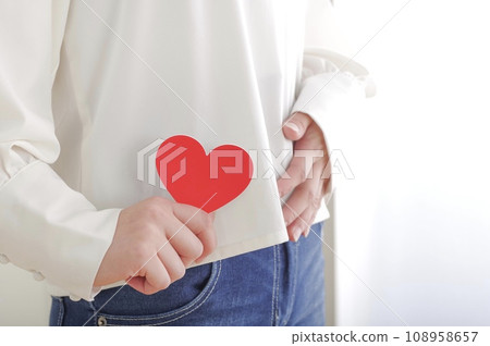 A woman holding a heart object and placing her hand on her lower abdomen A woman holding a heart object and placing her hand on her lower abdomen 108958657