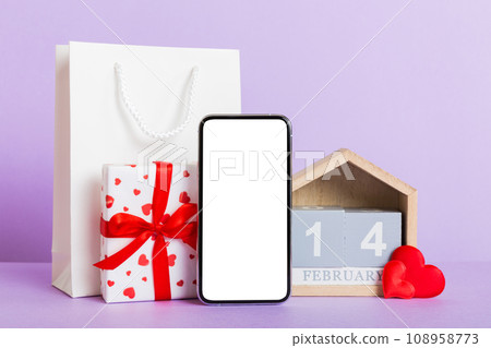 mobile phone with blank screen on colored background with hearts, calendar and gift box, valentine day 14 february concept perspertive view flat lay 108958773
