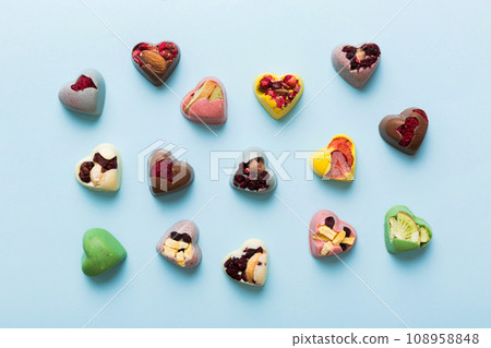 chocolate sweets in the form of a heart with fruits and nuts on a colored background. top view with space for text, holiday concept chocolate sweets in the form of a heart with fruits and nuts on a colored background. top view with space for text, holiday concept 108958848