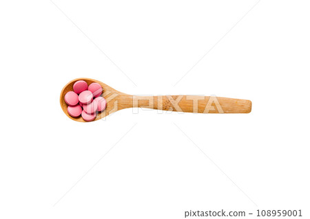 Vitamin capsules in a spoon on a colored background. Pills served as a healthy meal. Red soft gel vitamin supplement capsules on spoon 108959001