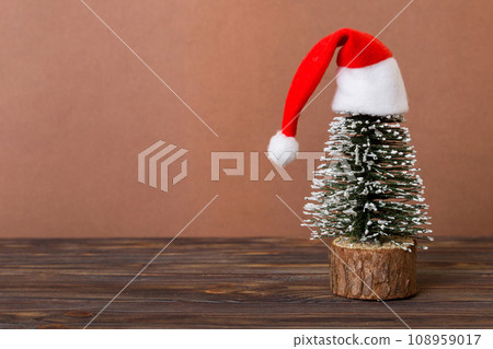 One small Christmas tree with santa hat on colored background. new year decoration with copy space One small Christmas tree with santa hat on colored background. new year decoration with copy space 108959017