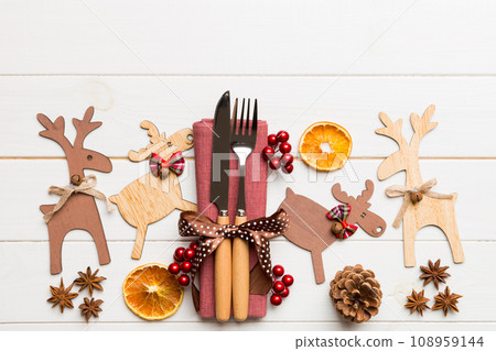 New year set of fork and knife on napkin. Top view of christmas decorations and reindeer on wooden background. Holiday family dinner concept with empty space for your design 108959144