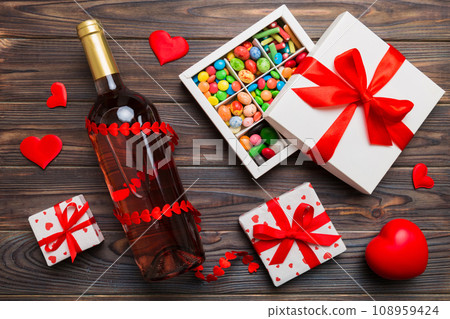 Bottle of red wine on colored background for Valentine Day with gift and chocolate. Heart shaped with gift box of chocolates top view with copy space Bottle of red wine on colored background for Valentine Day with gift and chocolate. Heart shaped with gift box of chocolates top view with copy space 108959424