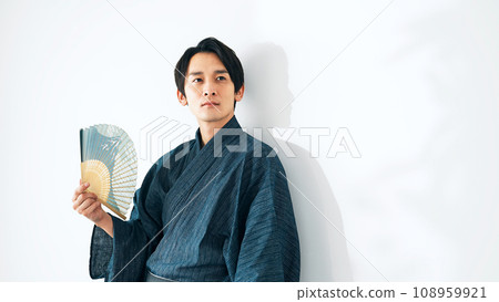 A man in Japanese clothes fanning himself with a folding fan A man in Japanese clothes fanning himself with a folding fan 108959921