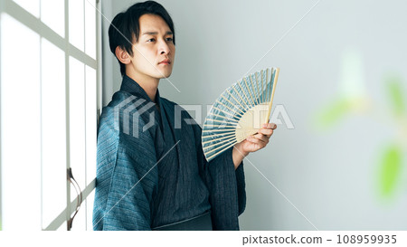 A man in Japanese clothes fanning himself with a folding fan A man in Japanese clothes fanning himself with a folding fan 108959935