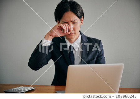 A young male office worker has itchy eyes and rubs them with his fingers A young male office worker has itchy eyes and rubs them with his fingers 108960245