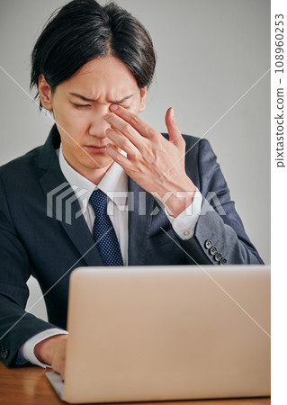 A young male office worker has itchy eyes and rubs them with his fingers A young male office worker has itchy eyes and rubs them with his fingers 108960253