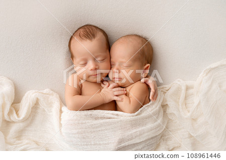 Tiny newborn twins boys in white cocoons on a white background. A newborn twin sleeps next to his brother. Newborn two twins boys hugging each other. Professional studio photography. Tiny newborn twins boys in white cocoons on a white background. A newborn twin sleeps next to his brother. Newborn two twins boys hugging each other. Professional studio photography. 108961446