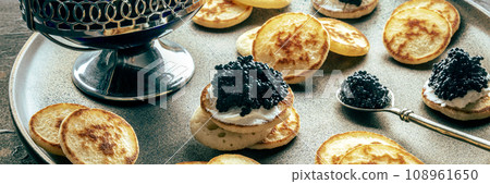 Blinis with black caviar panorama. Mini pancakes on a festive dish 108961650